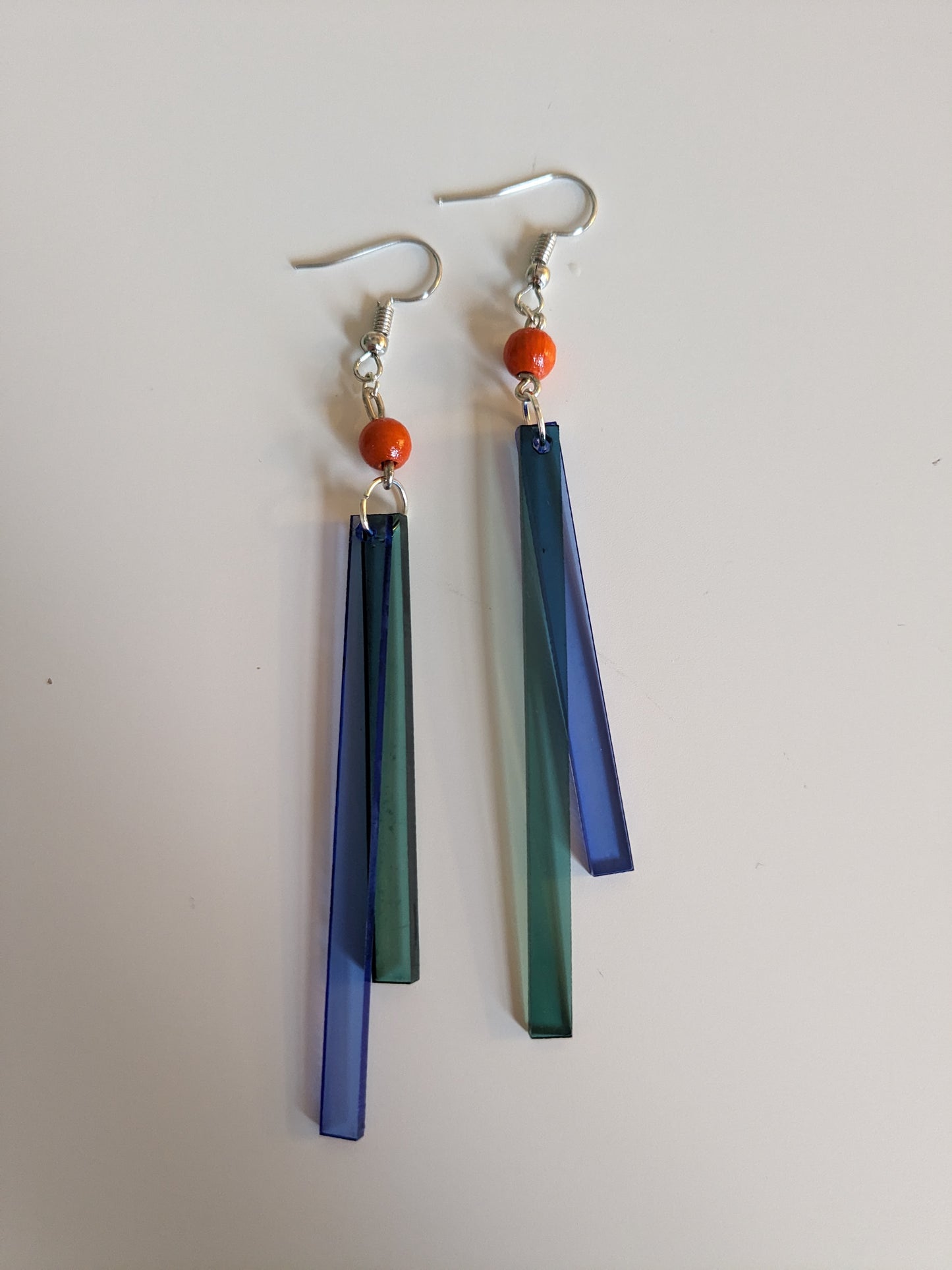 Colourful long dangle earrings made from blue and green acrylic bars and an orange wooden bead, with a new silver-plated wire. 