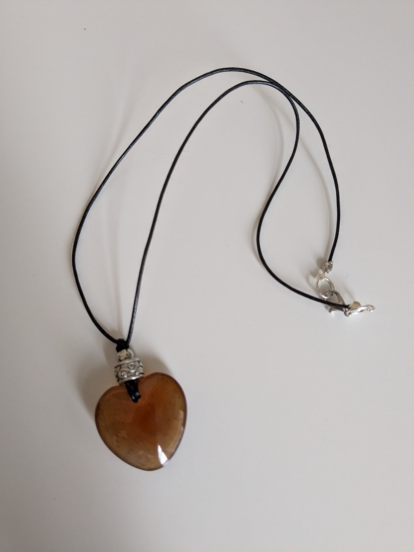 Retro necklace made with a large amber vintage glass heart charm and a patterned silver vintage bead on a faux leather cord.