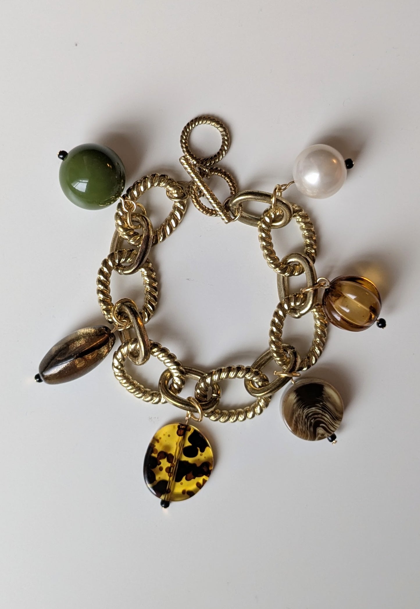 Chunky charm bracelet made with gold tone chain and a mix of earth tone vintage plastic and resin beads, with a ring and bar fastening. Adjustable to a smaller size (simply hook the clasp onto a different link).