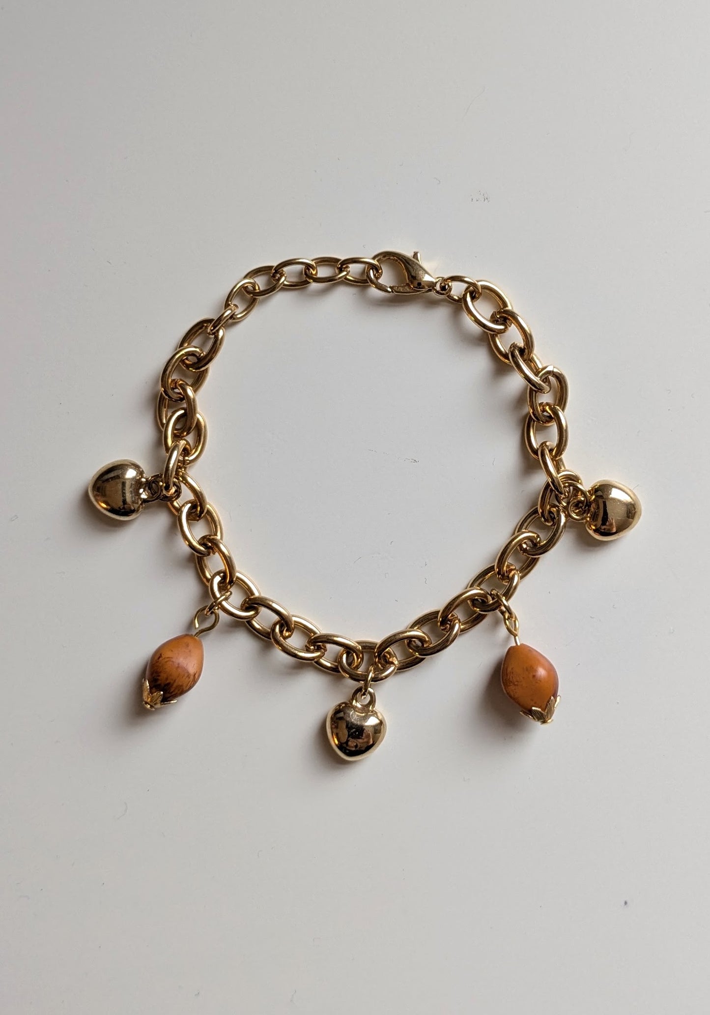 Cute charm bracelet, made with chunky gold tone chain, heavy gold tone heart charms, and vintage wooden acorn beads. Adjustable to a smaller size (simply hook the clasp onto a different link).