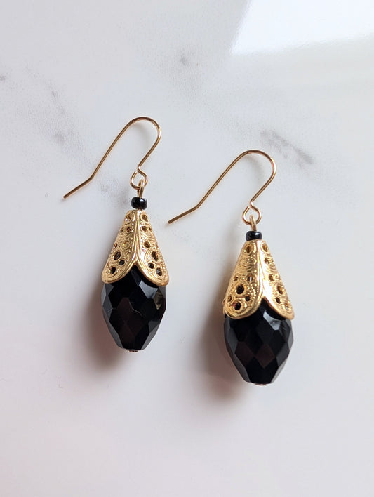 Pair of black teardrop earrings with gold filigree on a marble background