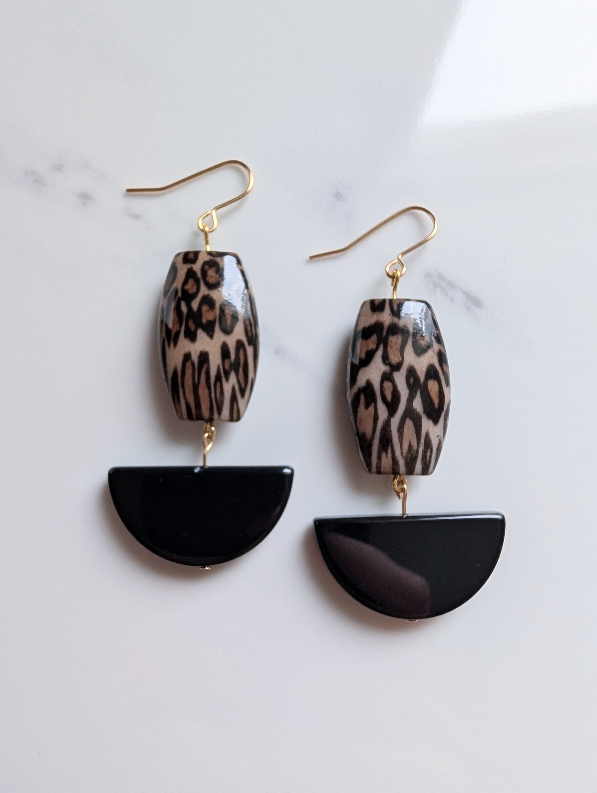 Pair of earrings with leopard print and black semi-circular designs on a marble surface.