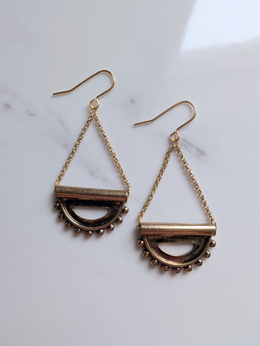 Pair of gold earrings with geometric eye design on a marble surface